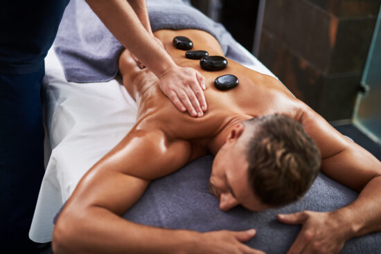 Professional masseur massaging client body while he lying on massage table