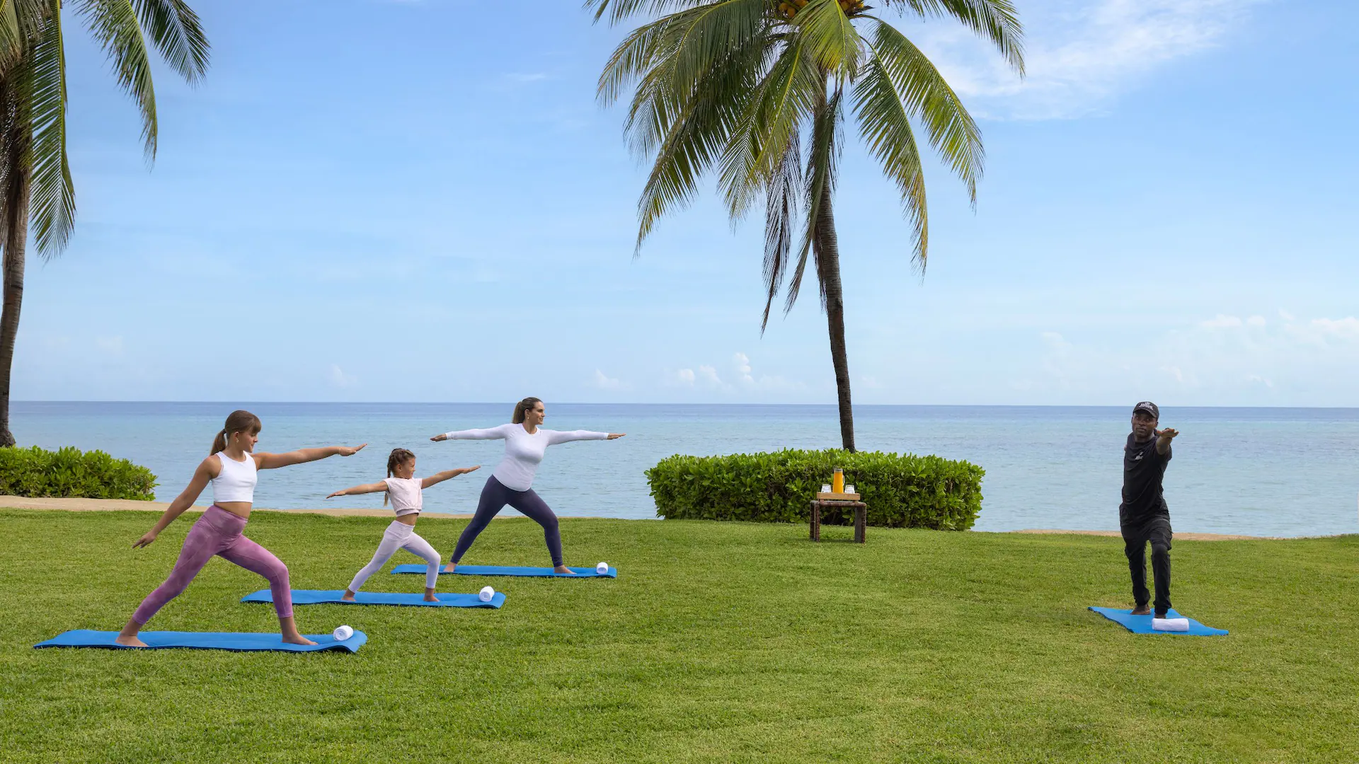 Mother and daughters practicing outdoor yoga by the ocean at Dreams Rose Hall Resort & Spa in Jamaica.