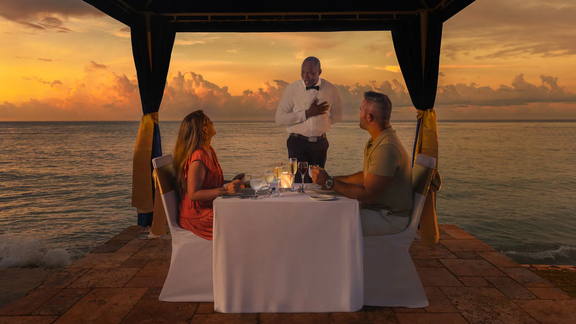 Couple enjoying a romantic sunset dinner by the ocean at Dreams Rose Hall Resort & Spa in Montego Bay, Jamaica.