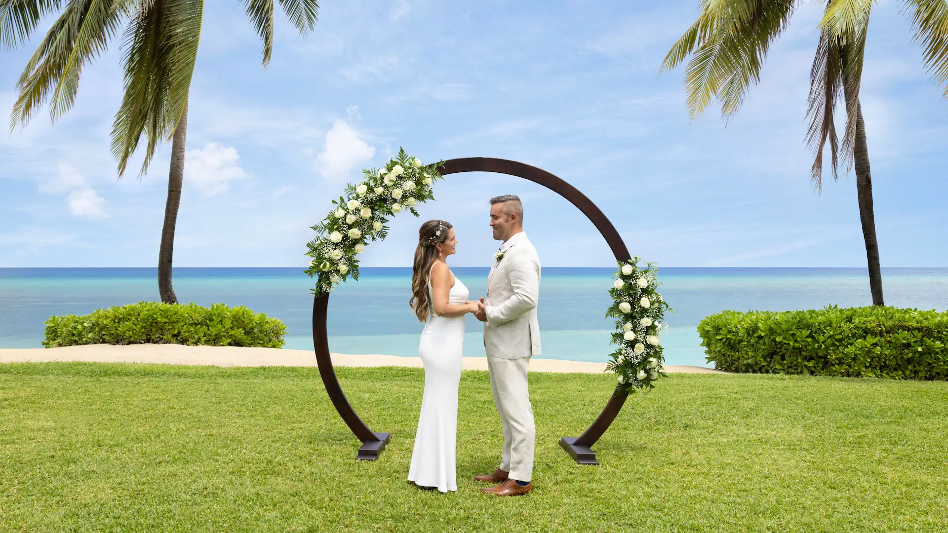 Bride and groom standing beneath a floral wedding arch overlooking the Caribbean Sea at Dreams Rose Hall Resort & Spa.