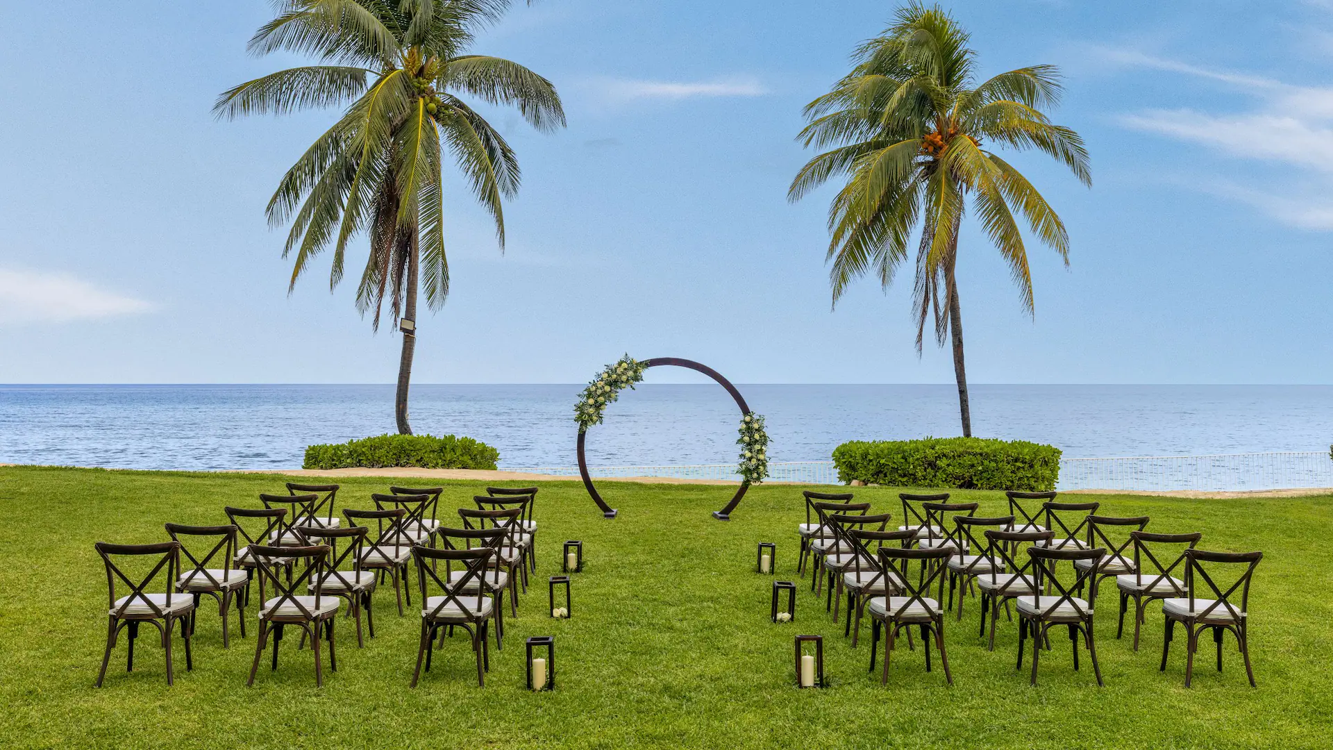 Oceanfront wedding ceremony setup with chairs and floral arch on the West Lawn at Dreams Rose Hall Resort & Spa.
